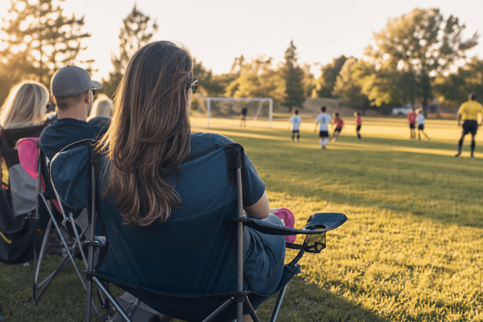 Parents watching their children play soccer from the sideline on a sunny afternoon